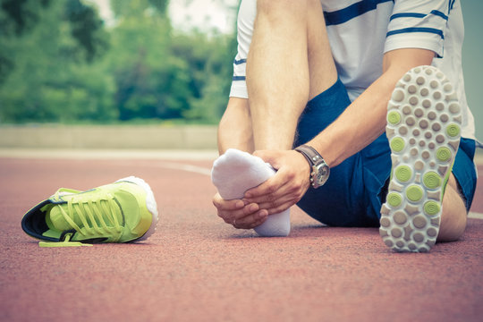 Jogger hands on foot. He is feeling pain as his ankle or foot is broken or twisted. Accident on running track during the morning exercise. Sport accident and foot sprain concepts.
