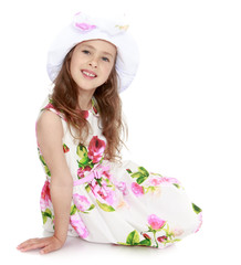 Charming little girl in a smart white dress with roses and a white cap , sitting on the floor - Isolated on white background