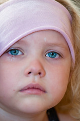 Caucasian little girl with blue eyes, curly blonde in a pink hat crying tears running down the face close-up