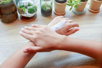 Young woman applying hands moisturizer lotion on wooden table