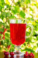 a glass of red cherry juice and cherries and red currants on a natural background. selective focus