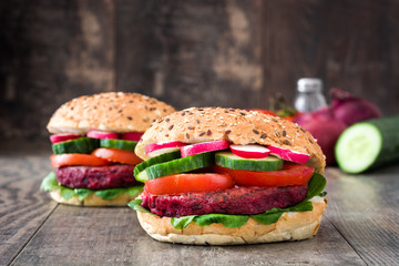 Veggie beet burger with lamb's lettuce, tomato, radish and cucumber on rustic wooden background

