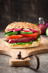 Veggie beet burger with lamb's lettuce, tomato, radish and cucumber on rustic wooden background

