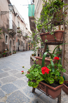 View of one characteristic street in Ortigia, the old part of Syracuse, with an ornamental wooden ladder and flowered vases