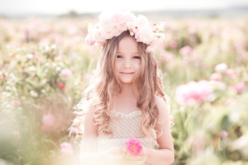 Smiling child girl 4-5 year old holding rose flower in meadow outdoors. Looking at camera. Childhood.
