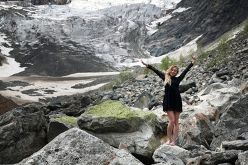 happy young blond woman in black dress among the huge stones on the glacier. Mestia
