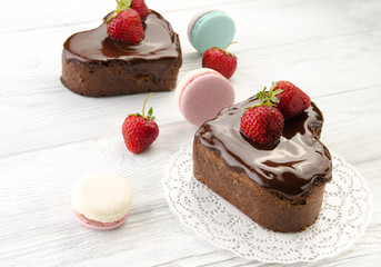 Heart cake with macarons.. Pieces of chocolate cake with fresh strawberry on wooden background. Top view.