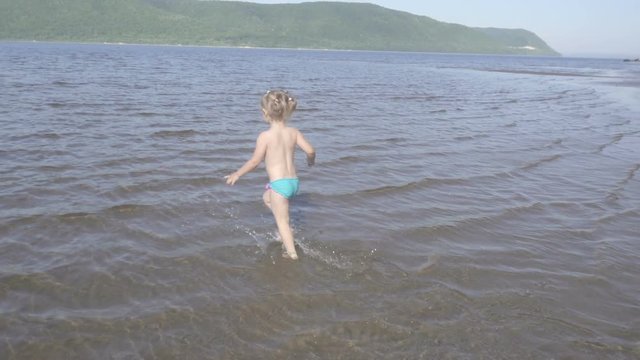 Slow motion. Little girl running, jumping, playing in the water. River bank, lake. laughter happiness