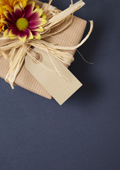 Floral gift border - Present wrapped in brown parcel paper with blank gift tag, raffia bow and red and yellow flower, arranged on a rustic slate background to form a page border