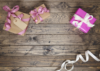 Gift wrap - Presents wrapped in brown parcel paper with pink satin bows, blank tag and white silk ribbon on a rustic wooden table top background forming a page border