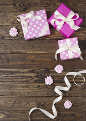 Gift wrap - Presents wrapped in pink wrapping paper with white silk ribbon bows and roses on a rustic wooden table top background forming a page border