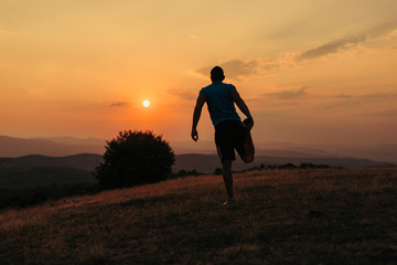 Silhouette of an athletic man in nature in front of a sunset while exercising