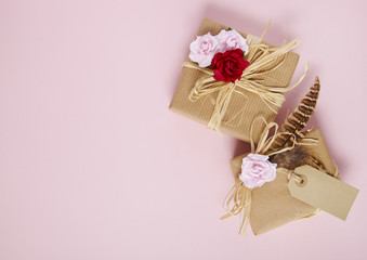 Gift wrap - Presents wrapped in brown parcel paper with raffia bows, blank tag, pink and red rose flowers and feathers on a pink background forming a page border