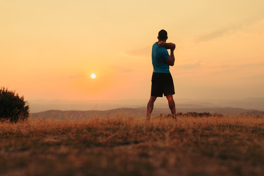 Silhouette of an athletic man in nature in front of a sunset while exercising