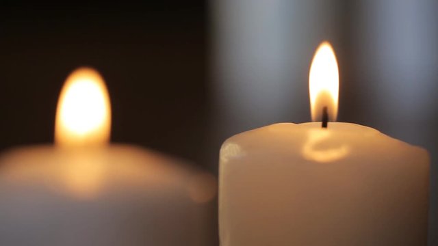 Two white candles burn in dark room to fill it with its light