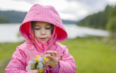 Outdoor portrait of cute little girl on the mountain picking up a bouquet of flowers