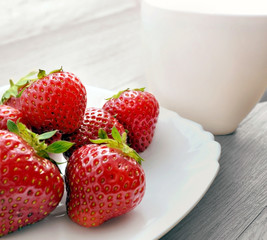 
The photo ripe strawberries in a white plate with a cup