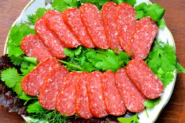 Нарезка колбасы лежит на тарелке с зеленью