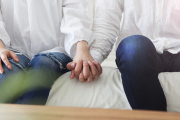 Fototapeta premium Young couple holding hands sitting on the sofa