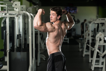 Fototapeta na wymiar Muscular Man Flexing Biceps Muscles In Gym