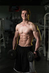 Obraz na płótnie Canvas Young Man With Dumbbells Exercising Biceps