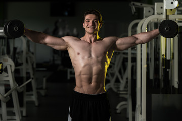Fototapeta na wymiar Young Man With Dumbbells Exercising Shoulders