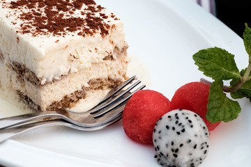 Tiramisu on white plate with melon, mint and, dragon fruit