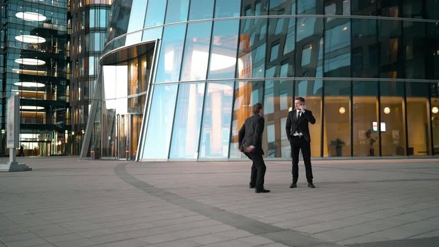 Funny joke. Young businessman have a smartphone talking. Goof stupid competitor running and giving kick ass to suit clothes man and runs away. Businessman overtake rival. Glossy business centre