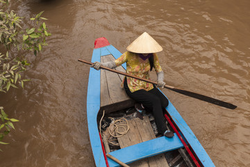 Obraz premium Vietnamese woman row on a wood boat in muddy tributary of Mekong river
