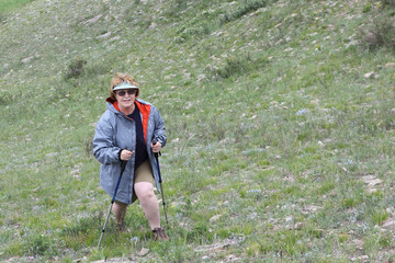 Fototapeta na wymiar The adult smiling woman rising uphill with tracking sticks