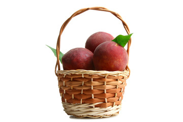 a bunch of delicious and juicy peaches with green leaves on white isolated background in the wicker basket