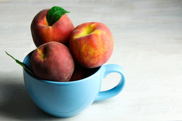 delicious and juicy peaches with green leaves in a blue Cup on white wooden background