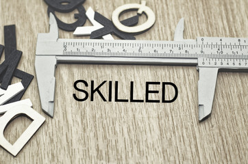 Business motivation and finance concept, vernier caliper with word SKILLED over wooden floor and...