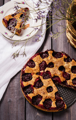 Plum pie with nuts sliced on a dark wooden background 