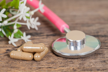 herb capsules and stethoscope on wood table