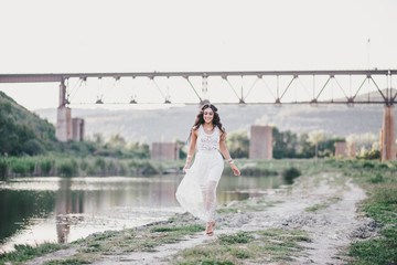 Beautiful young woman with long curly hair dressed in boho style dress posing near lake