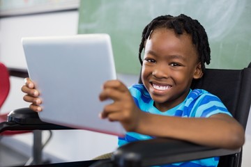 Schoolboy sitting on wheelchair and using digital tablet
