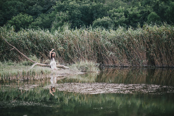 Beautiful young woman with long curly hair dressed in boho style dress posing near lake