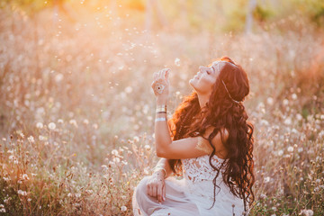 Beautiful young woman with long curly hair dressed in boho style dress posing in a field with...
