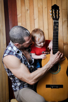 Little baby girl with his hipster father playing guitar on wooden background