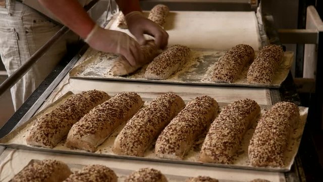 Bakers putting the raw baguettes with seeds to the baking sheet