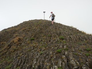 Hiker climbing on sharp peak of basalt formation of volcano