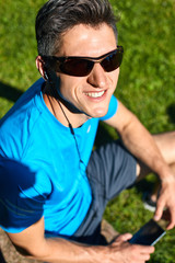 Fototapeta premium athlete sitting with bottle of water and mobile phone on the stone in the park