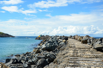 Rustic, old wooden track leading out to colorful blocks on a harbor breakwater near Coffs Harbour, New South Wales, Australia