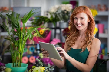 Abwaschbare Fototapete Blumenladen Lächelnde Floristin mit digitalem Tablet im Blumenladen