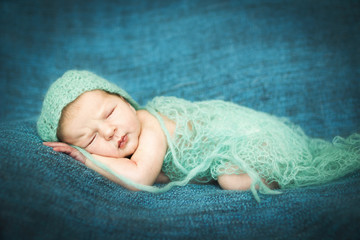 newborn baby sleeping sweetly on a blue rug in blue cap