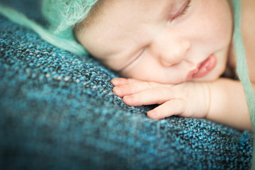newborn baby sleeping sweetly on a blue rug in blue cap
