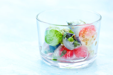 Fresh fruits and berry frozen in ice cubes on blue background