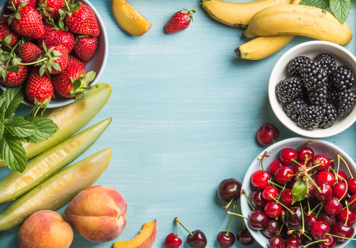 Healthy summer fruit variety. Sweet cherries, strawberries, blackberries, peaches, bananas, melon slices and mint leaves on blue backdrop