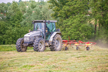 Farmer driving a tractor on the field with the attached tool used to spread hay on the field